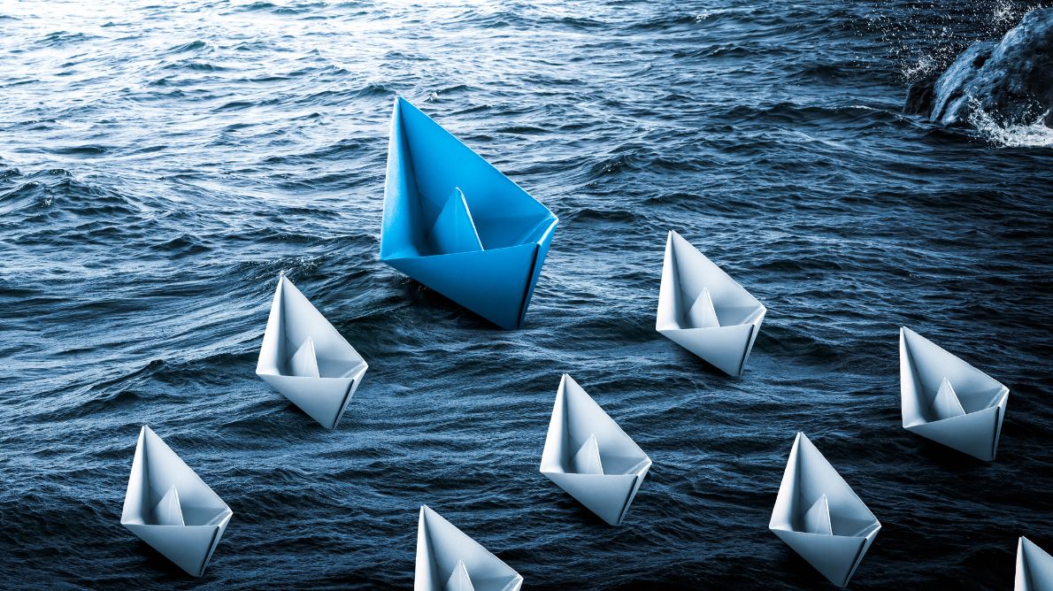 white paper boats on the sea heading in the same direction lead by blue boat